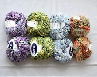 May include: Assortment of eight colourful yarn skeins in various textures, including fuzzy, smooth, and textured. The skeins are arranged in a semi-circle on a white surface. The yarn is labelled "Polo" on several of the skeins.