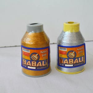 May include: Two spools of gold and silver embroidery thread with the brand name "YABALI" and the text "NAKIŞ SİMİ" on the labels.