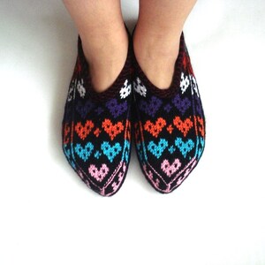 May include: A pair of black knitted slippers with a colorful heart pattern in shades of pink, blue, orange, and white.