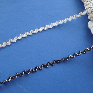 May include: Two spools of decorative trim, one white with gold accents and one black with silver accents. Both trims have a wavy, zig-zag pattern.