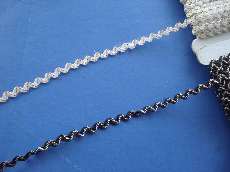 May include: Two spools of decorative trim, one white with gold accents and one black with silver accents. Both trims have a wavy, zig-zag pattern.