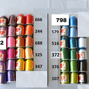 May include: A collection of spools of thread in various colors, including red, orange, yellow, green, blue, and purple. The spools are arranged in rows and labeled with numbers, such as 602, 340, 917, 550, 666, 244, 688, 325, 347, 798, 579, 516, 372, 376, 107, and 896. The spools are all the same size and shape, and they are arranged in a neat and orderly fashion.