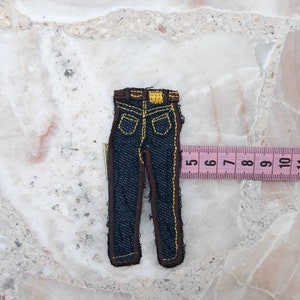 Könnte beinhalten: Ein blauer Jeans-Patch mit braunen Nähten und einem gelben Etikett. Der Patch ist etwa 5 cm hoch.