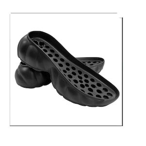Puede incluir: Un par de plantillas para zapatos negras con una superficie texturizada y un patrón de pequeños agujeros. Las plantillas están diseñadas para brindar soporte y comodidad.