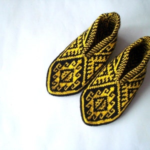 May include: A pair of knitted slippers with a geometric pattern in black and yellow. The slippers have a closed-toe design and are made of a soft, textured yarn. The pattern is repeated throughout the slipper.