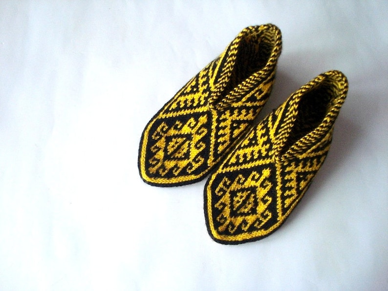 May include: A pair of knitted slippers with a geometric pattern in black and yellow. The slippers have a closed-toe design and are made of a soft, textured yarn. The pattern is repeated throughout the slipper.
