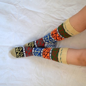 May include: A pair of colorful knitted socks with geometric patterns in shades of blue, orange, red, yellow, and green. The socks have a beige cuff.
