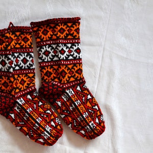 May include: Pair of hand-knitted wool socks with a geometric pattern in orange, red, black, and white.