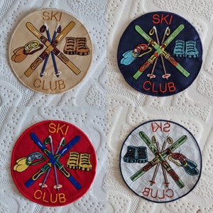 May include: Four embroidered patches with a ski club theme. Each patch features a pair of skis crossed with ski poles, a pair of ski boots, and the text "SKI CLUB". The patches are in different colours: blue, red, white, and black.