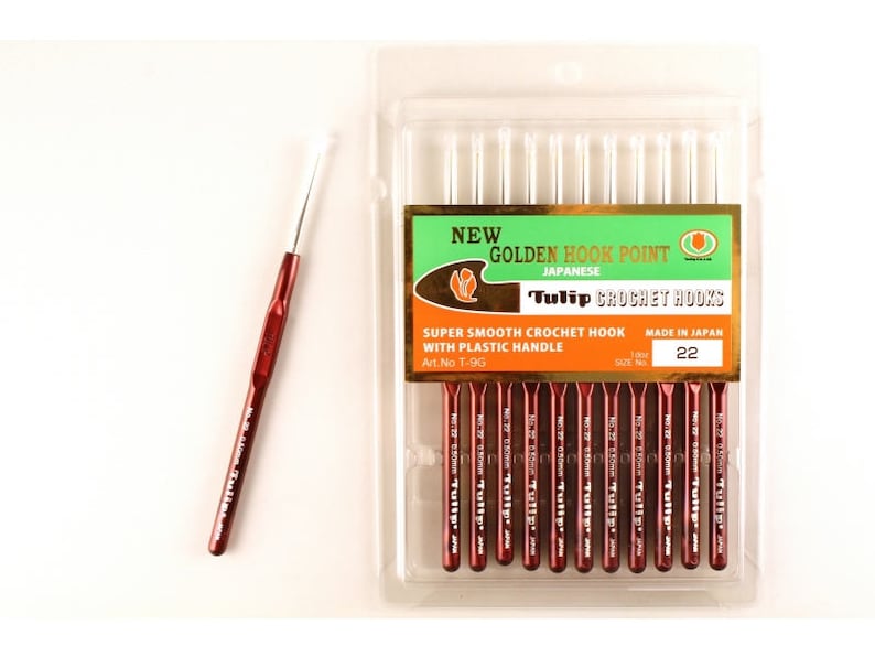 May include: A package of 10 Tulip brand crochet hooks, size 22, with golden hook points and plastic handles. The package is labeled "New Golden Hook Point Japanese Tulip Crochet Hooks Super Smooth Crochet Hook with Plastic Handle Art. No T-9G Made in Japan Size No 22".