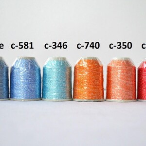 May include: Six spools of metallic thread in various colors, including blue, turquoise, orange, and red. The spools are labeled with color codes, such as "c-581" and "c-346".