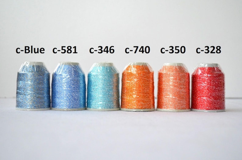 May include: Six spools of metallic thread in various colors, including blue, turquoise, orange, and red. The spools are labeled with color codes, such as "c-581" and "c-346".