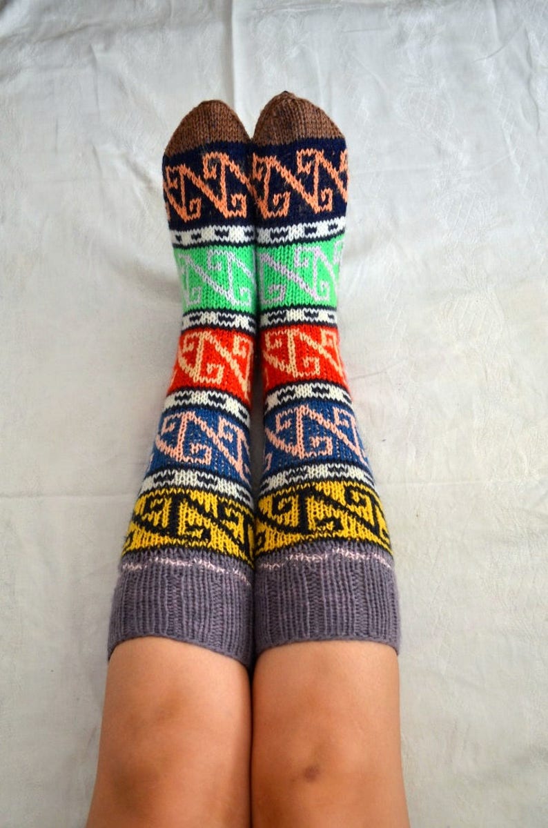 May include: A pair of colorful knitted socks with a geometric pattern in shades of brown, orange, yellow, green, blue, and pink. The socks are made of a soft, warm material and are perfect for keeping your feet cozy in the winter.