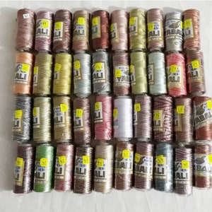 May include: A selection of thread spools in a variety of colours, each marked with the brand name "ALI" and a weight of 25g. The threads range from pink and green to brown and white, ideal for crafting and sewing.