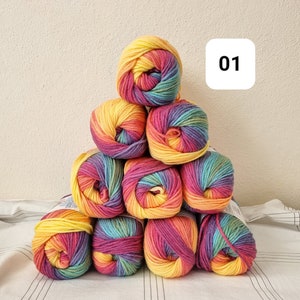 May include: A pyramid of ten colorful yarn skeins. Each skein displays a gradient of rainbow colors, including yellow, orange, red, pink, purple, blue, and green. The number "01" is in a white square in the background. The yarn is arranged on a white and gray striped surface.