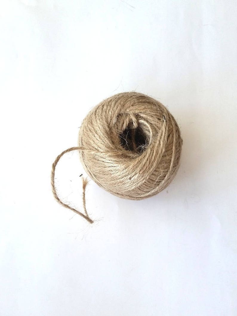 May include: A ball of natural twine, made from jute, is shown on a white background. The twine is brown and has a rough texture. The twine is unraveled and the end is visible.
