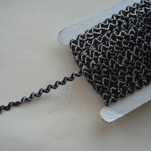 May include: Black and silver trim with a wavy texture. The trim is on a white card.