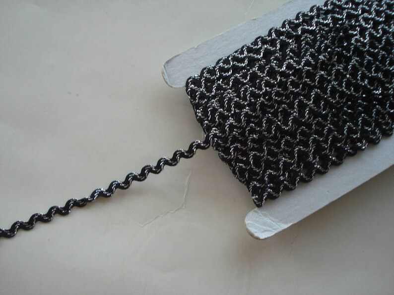 May include: Black and silver trim with a wavy texture. The trim is on a white card.