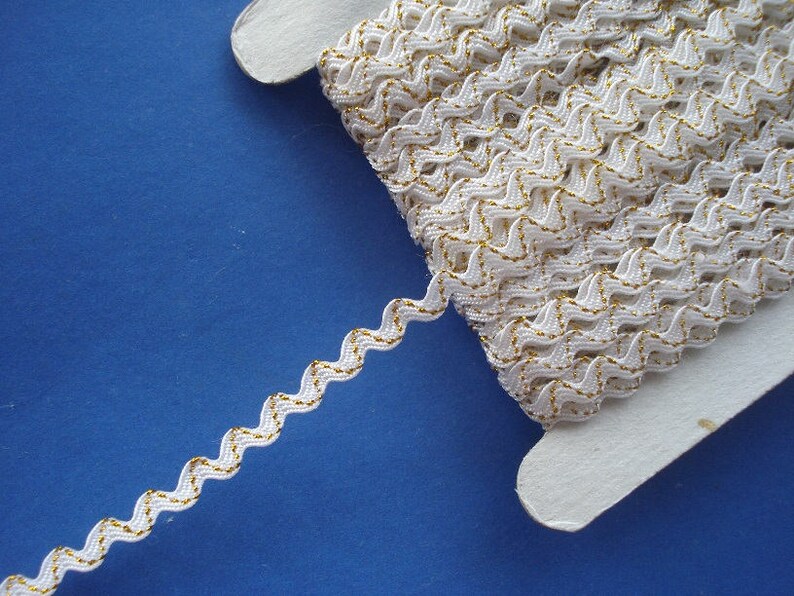 May include: White zig zag trim with a gold metallic thread running through it. The trim is wound around a white cardboard spool.