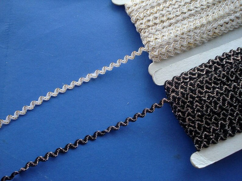 May include: Two spools of trim, one white with gold thread and one black with silver thread. Both trims have a wavy, zig-zag pattern.