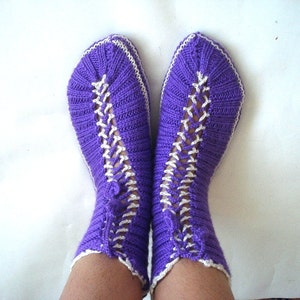 May include: Purple knitted socks with white knit detailing. The socks are folded down at the top and have a lace-like pattern.