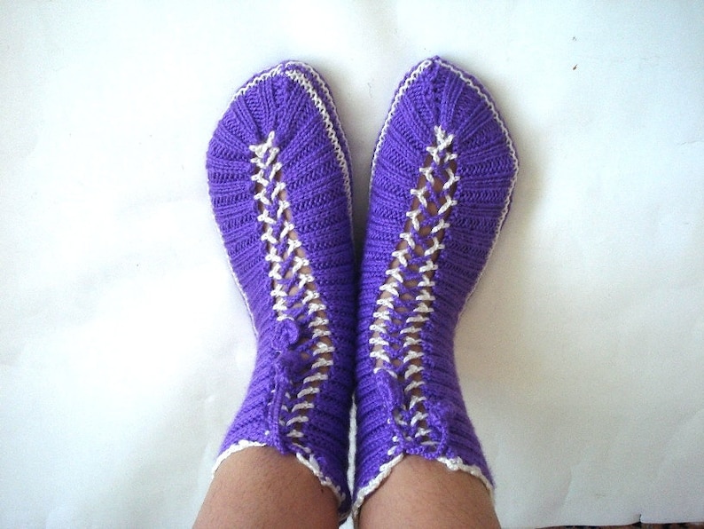 May include: Purple knitted socks with white knit detailing. The socks are folded down at the top and have a lace-like pattern.