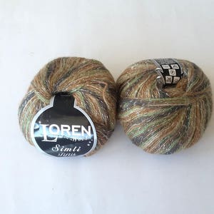 Puede incluir: Dos ovillos de lana en colores verde, marr&oacute;n y dorado con purpurina plateada. La lana est&aacute; etiquetada como "Loren Wool Simli Tiftik".