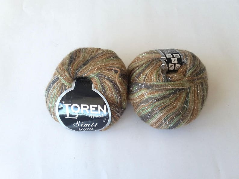 Puede incluir: Dos ovillos de lana en colores verde, marr&oacute;n y dorado con purpurina plateada. La lana est&aacute; etiquetada como "Loren Wool Simli Tiftik".