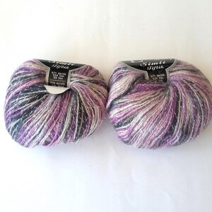 Puede incluir: Dos ovillos de hilo de color morado, blanco y gris con purpurina plateada. El hilo est&aacute; etiquetado como "Simli Iplik" y tiene el texto "5271 Acrylic 32/2 50 gr 75% Acrylic 25% Wool".