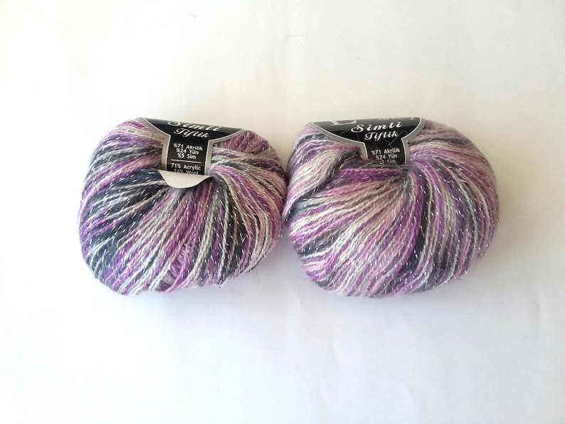Puede incluir: Dos ovillos de hilo de color morado, blanco y gris con purpurina plateada. El hilo est&aacute; etiquetado como "Simli Iplik" y tiene el texto "5271 Acrylic 32/2 50 gr 75% Acrylic 25% Wool".