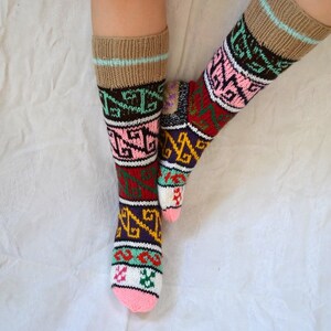May include: A pair of colorful knitted socks with geometric patterns in shades of pink, green, red, yellow, and brown. The socks are worn on a person's legs.