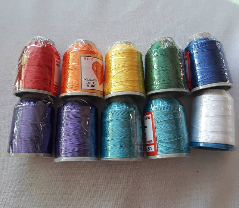 May include: Assortment of ten spools of thread in various colors, including red, orange, yellow, green, blue, purple, turquoise, and white. The spools are labeled "No. 50" and "Polyester Dantel Ipligi".