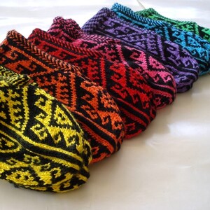 May include: A collection of colorful knitted slipper socks. Each sock features a geometric pattern in a vibrant color combination, including yellow, orange, red, pink, purple, blue, and green, all with black accents. The socks are arranged in a row.