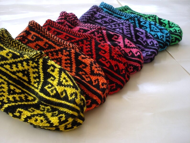 May include: A collection of colorful knitted slipper socks. Each sock features a geometric pattern in a vibrant color combination, including yellow, orange, red, pink, purple, blue, and green, all with black accents. The socks are arranged in a row.