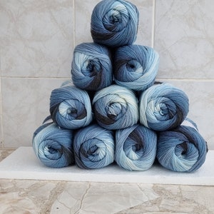 May include: A stack of ten balls of yarn in shades of blue, white, and black. The yarn is arranged in a pyramid shape.
