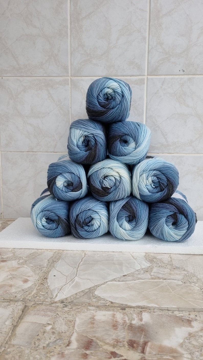 May include: A stack of ten balls of yarn in shades of blue, white, and black. The yarn is arranged in a pyramid shape.