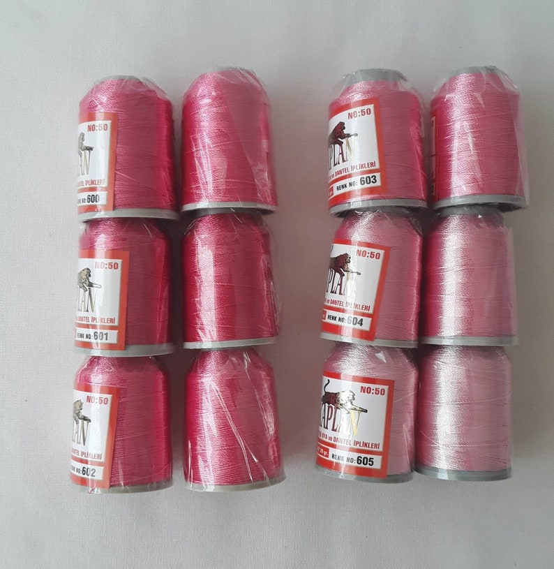 May include: Twelve spools of pink thread, each wrapped in clear plastic. The spools are labeled "NO:50" and "APLAN" with a number from 600 to 605.