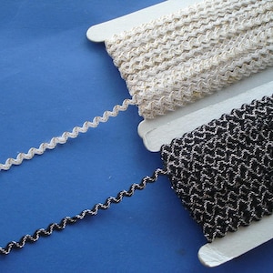 May include: Two spools of trim, one white and one black, with a wavy, zig-zag pattern. Both trims have a metallic sheen.