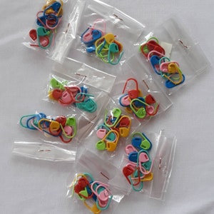 Puede incluir: Varias bolsas de marcadores de punto de plástico de colores, también conocidos como marcadores de punto de bloqueo, para tejer y hacer ganchillo. Los marcadores son de varios colores, incluidos rojo, verde, azul, amarillo, rosa y naranja.