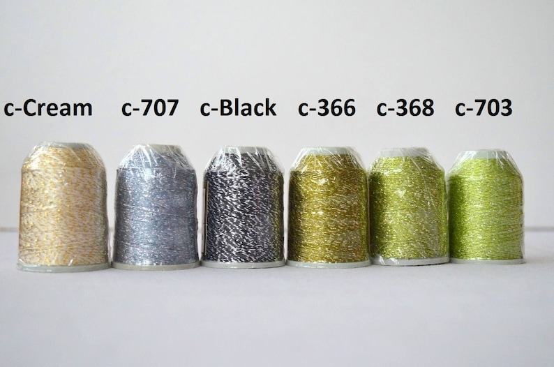 May include: Six spools of metallic thread in various colors, including cream, silver, black, gold, green, and lime green. The spools are labeled with their color codes: c-Cream, c-707, c-Black, c-366, c-368, and c-703.