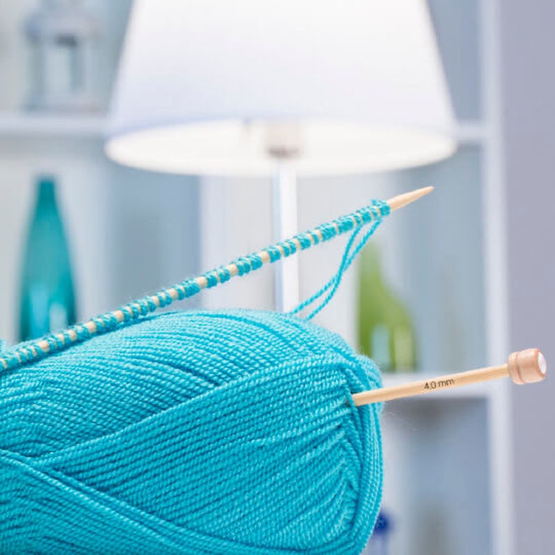 May include: A close-up of a ball of turquoise yarn with knitting needles. One needle is inserted into the yarn, and the other holds a row of knitted stitches. The needles are made of light-colored wood. The needle in the yarn has the text "4.0 mm".