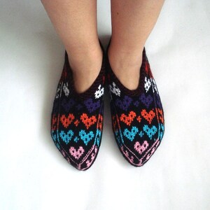 May include: A pair of black knitted slippers with a colorful heart pattern. The pattern features pink, blue, orange, and purple hearts.