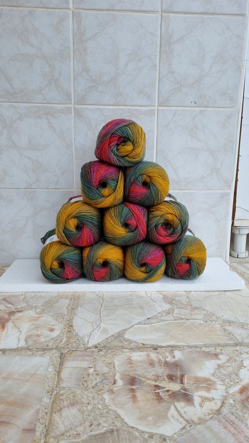 May include: A stack of nine balls of yarn in a triangular shape. The yarn is a mix of green, yellow, and red.