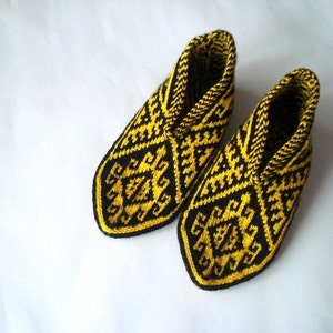May include: A pair of knitted slippers with a geometric pattern in black and yellow. The slippers have a closed-toe design and a high ankle cuff. The pattern features repeating diamond and zigzag shapes.