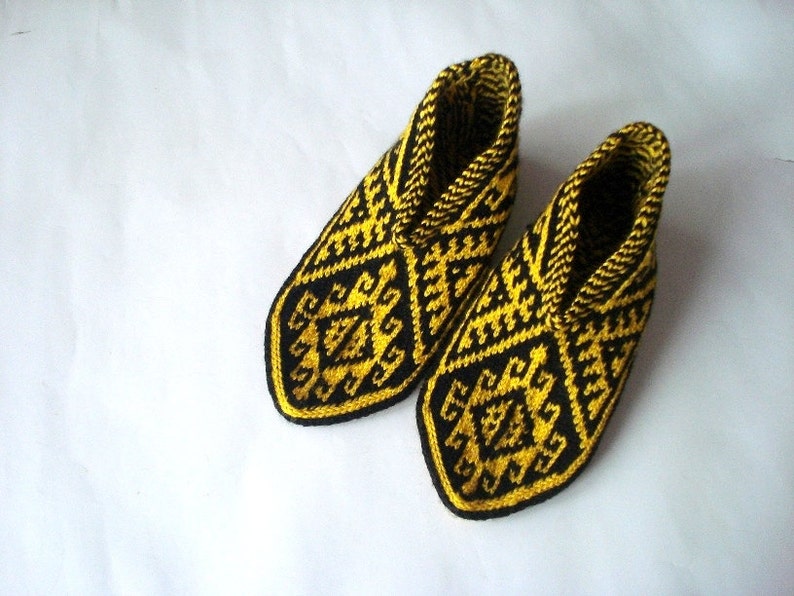 May include: A pair of knitted slippers with a geometric pattern in black and yellow. The slippers have a closed-toe design and a high ankle cuff. The pattern features repeating diamond and zigzag shapes.