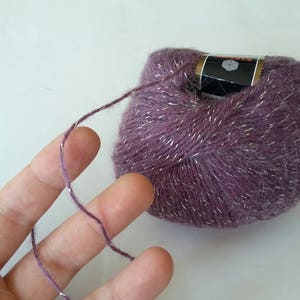 Puede incluir: Un ovillo de hilo morado con hilo plateado que lo atraviesa. El hilo est&aacute; envuelto alrededor de una etiqueta que dice "Katia"