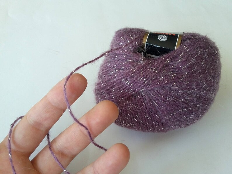 Puede incluir: Un ovillo de hilo morado con hilo plateado que lo atraviesa. El hilo est&aacute; envuelto alrededor de una etiqueta que dice "Katia"