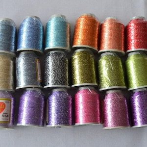 May include: Assortment of 18 spools of metallic embroidery thread in various colors, including gold, silver, blue, green, pink, and red. The spools are arranged in three rows of six. The brand name "Candy Chic" is visible on one of the spools.