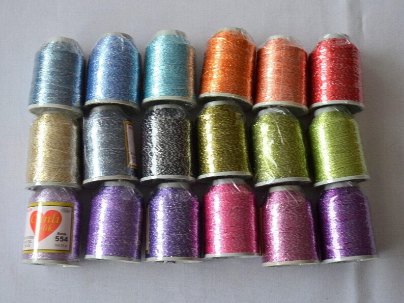 May include: Assortment of 18 spools of metallic embroidery thread in various colors, including gold, silver, blue, green, pink, and red. The spools are arranged in three rows of six. The brand name "Candy Chic" is visible on one of the spools.