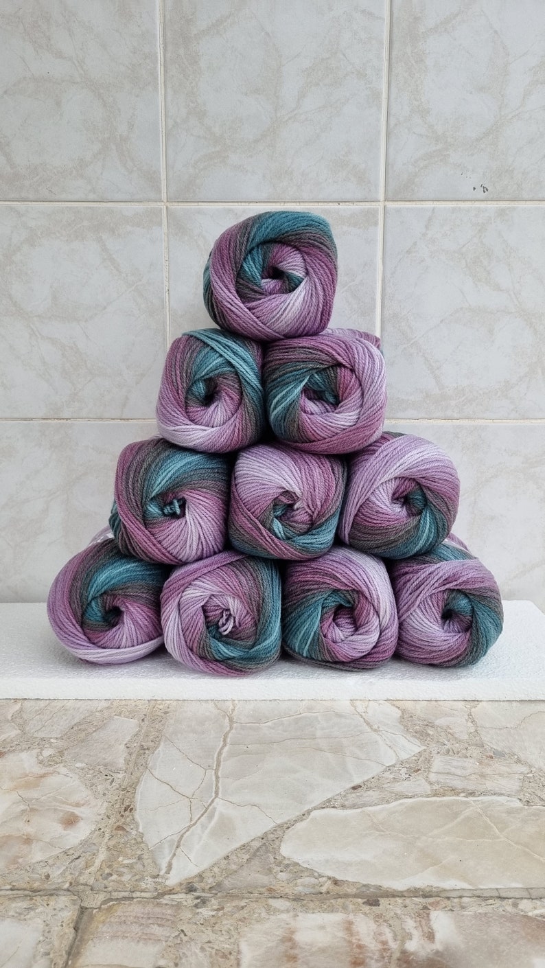 May include: A stack of ten balls of yarn in shades of purple, green, and brown. The yarn is arranged in a pyramid shape.